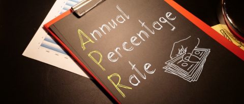 The words “Annual Percentage Rate” drawn on a chalkboard with drawing of hand holding money. 