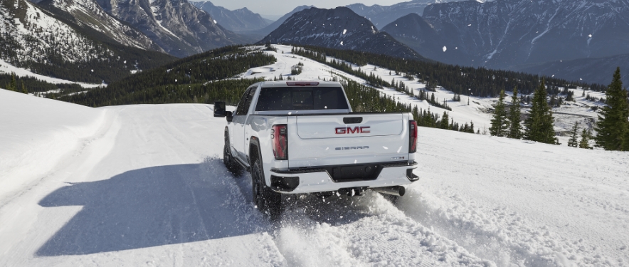 Winterized white GMC Sierra driving through the snow on a mountain road.