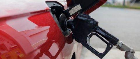 Close-up of gasoline nozzle filling up a red GM vehicle. 