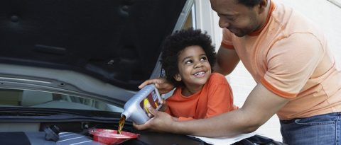 Padre mostrándole a su hijo cómo colocar aceite de motor en un vehículo