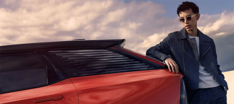 A man with shades leans against a red vehicle