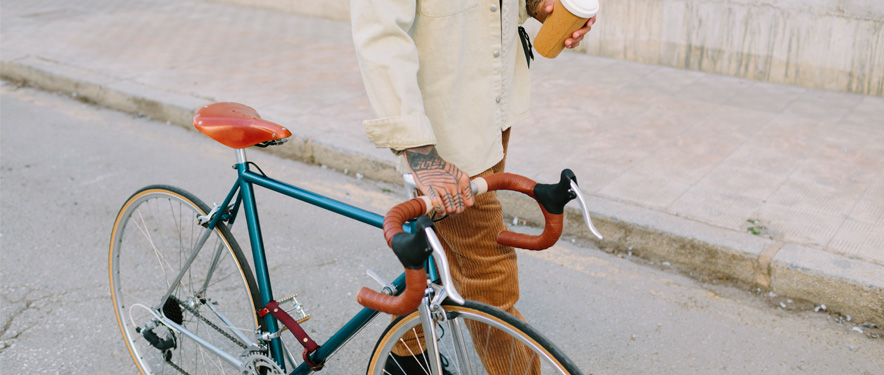 Person with hand tattoos walking road bike down a street