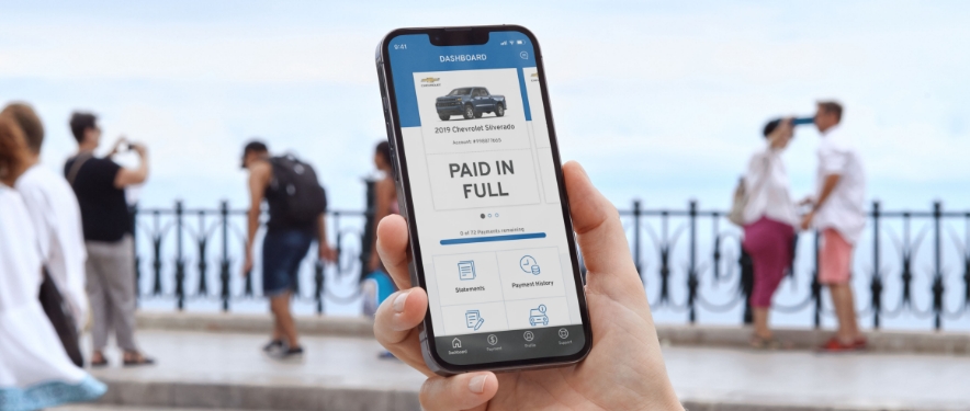 Person on a boardwalk holding up a phone displaying the GM Financial Mobile app.