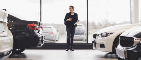 Woman standing in a well-lit showroom pondering things to consider before leasing a vehicle.