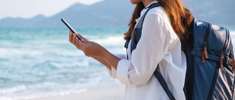 Backpacker checking her MyAccount on the GM Financial Mobile app while standing on a beach.