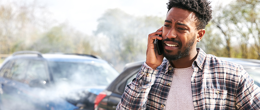 Concerned man making a phone call standing in front of a wrecked car.