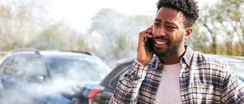 Concerned man making a phone call standing in front of a wrecked car.