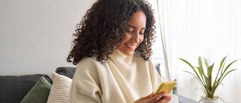 Woman sitting on couch looking at auto insurance premiums on her phone.