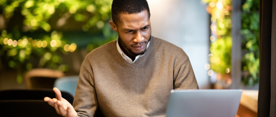 A cautious person at their laptop, looking skeptical while reading an email.