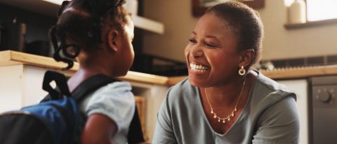 Smiling mother saying goodbye to a young elementary school student with a backpack.