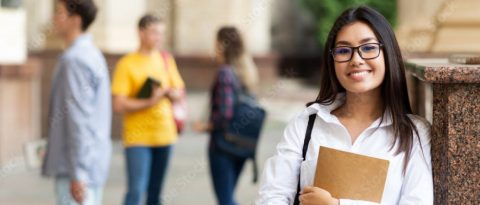 Smiling student walking on campus, with other students chatting in the background.
