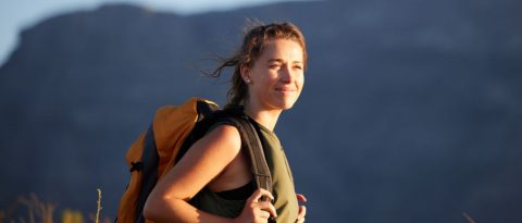 Smiling woman with backpack on a hiking trip she paid for by investing.